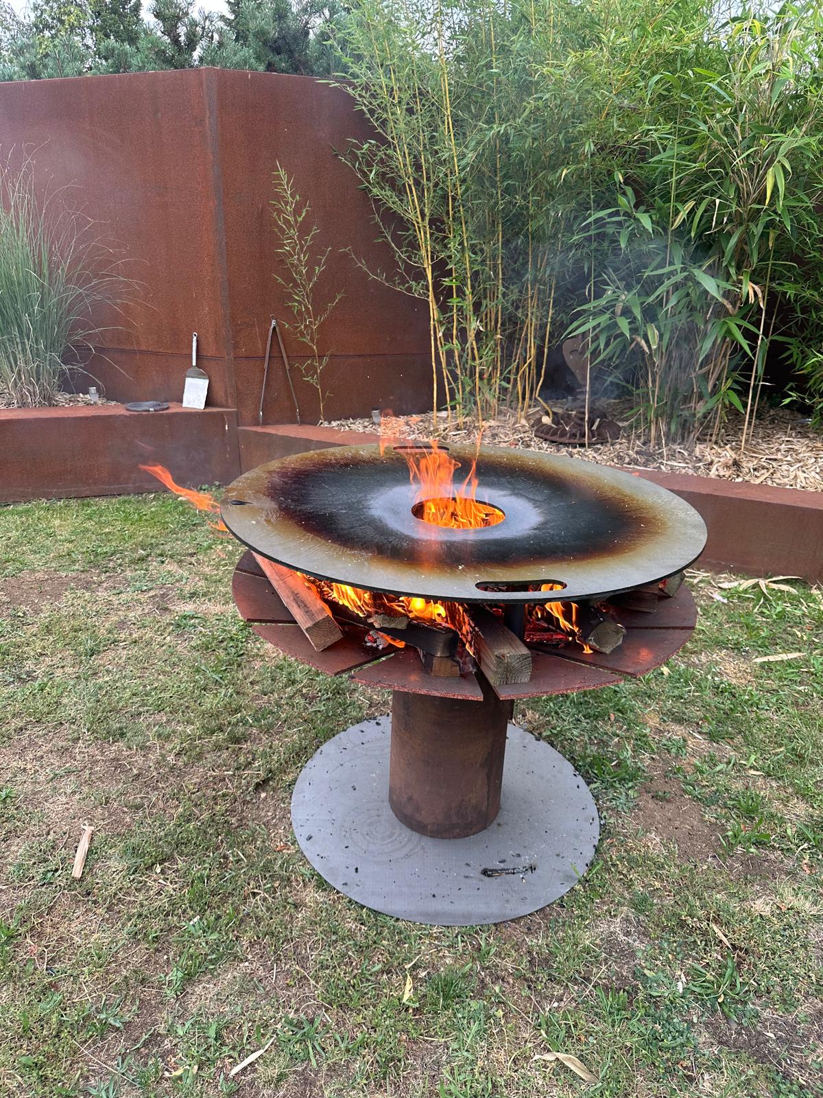 Feuerplatte auf Feuerschale mit Grilleinsatz und zentraler Hitzezone im Garten